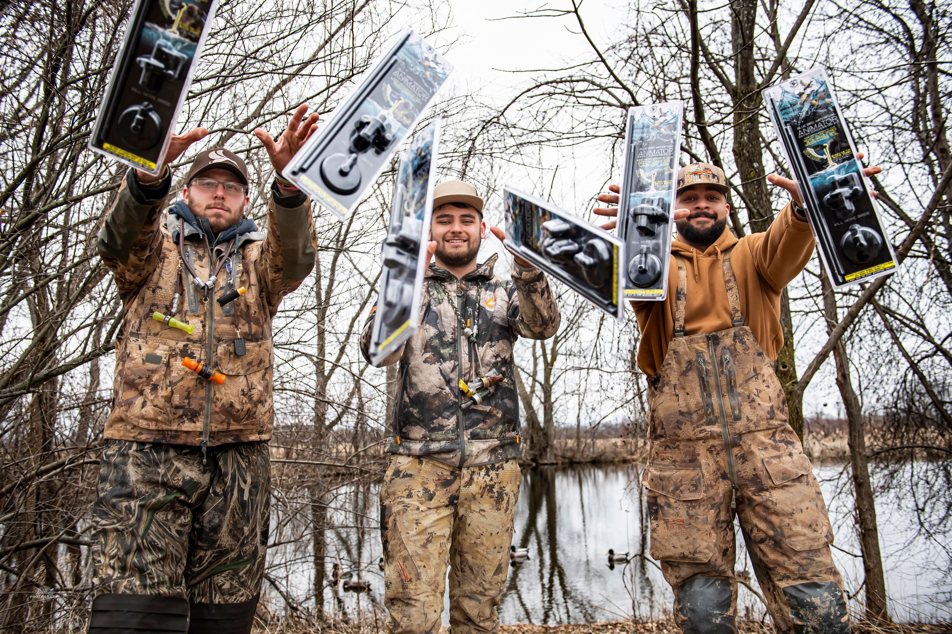 Three men in camouflage clothing holding blue bird waterfowl animators in packages in a forest setting.